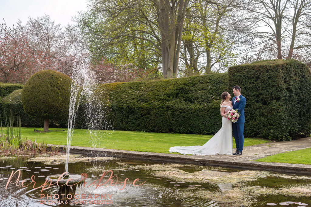 Photo of bride and groom stood in fornt of a pond on their wedding day in Milton keynes