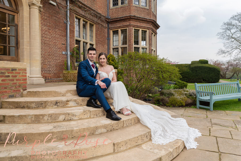 Photo of bride and groom sat on steps outside their wedding venue in Milton Keynes