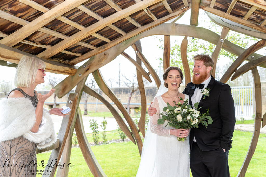 Photograph of a bride and groom under a gazebo listening to a reading on their wedding day in Milton Keynes