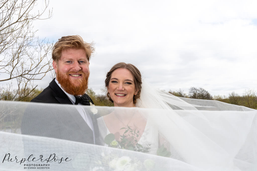 Photograph of a brides wedding veil swirling around the couple at their wedding in Milton Keynes