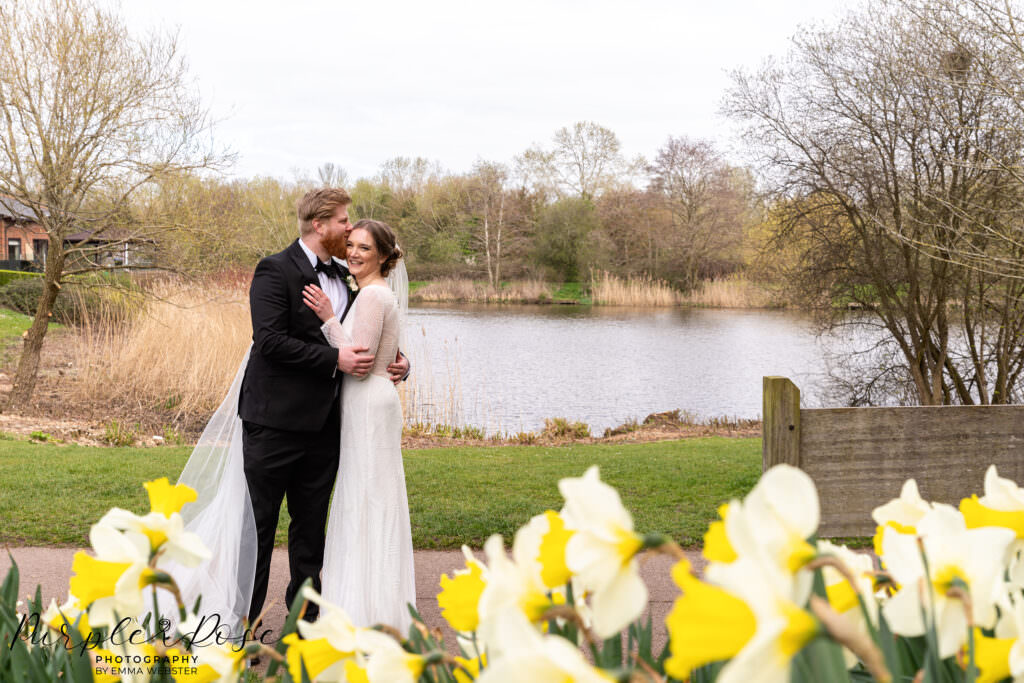 Bride and groom in front of daffodils at a lake side in Milton Keynes
