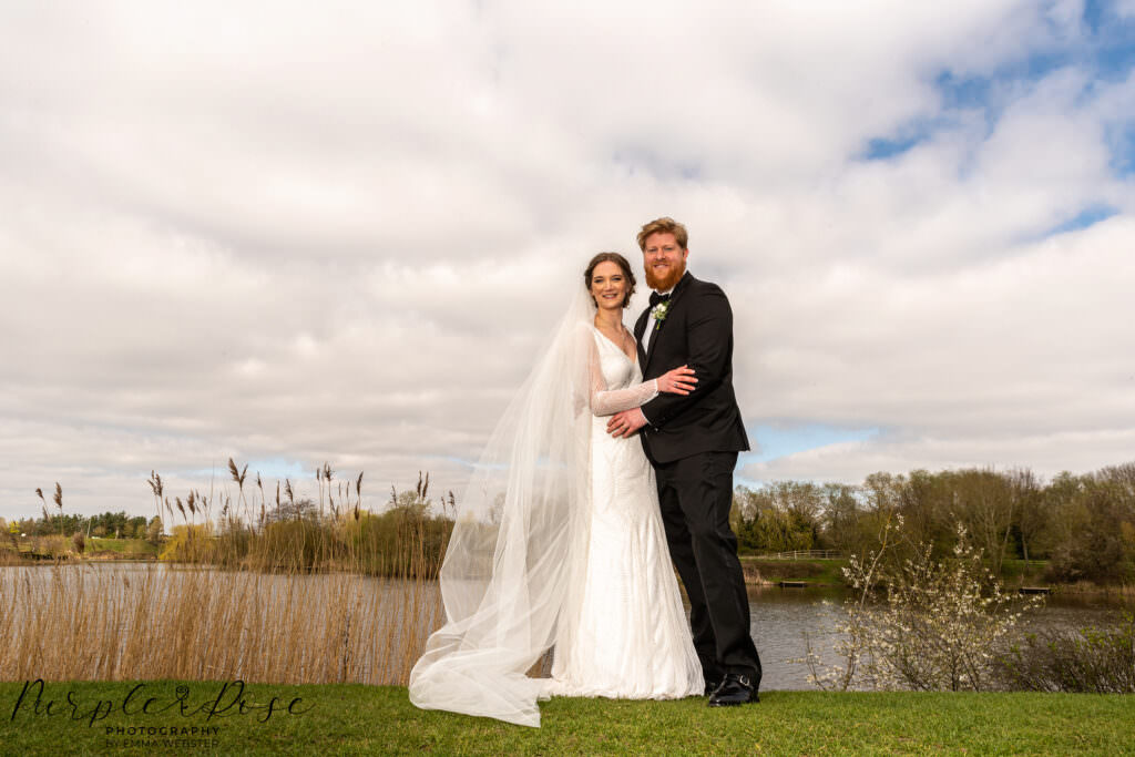 Bride and groom stood by a lake side on their wedding day in Milton Keynes