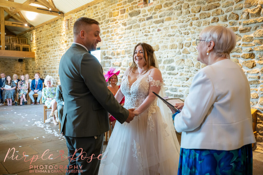 Bride and groom holdng hands and laughing during their wedding ceremony at Dodford Manor