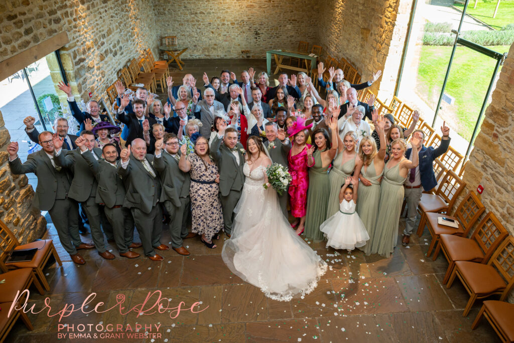 Group photo of all the wedding guests taken from the balcony in the barn at Dodford Manor in Northampton