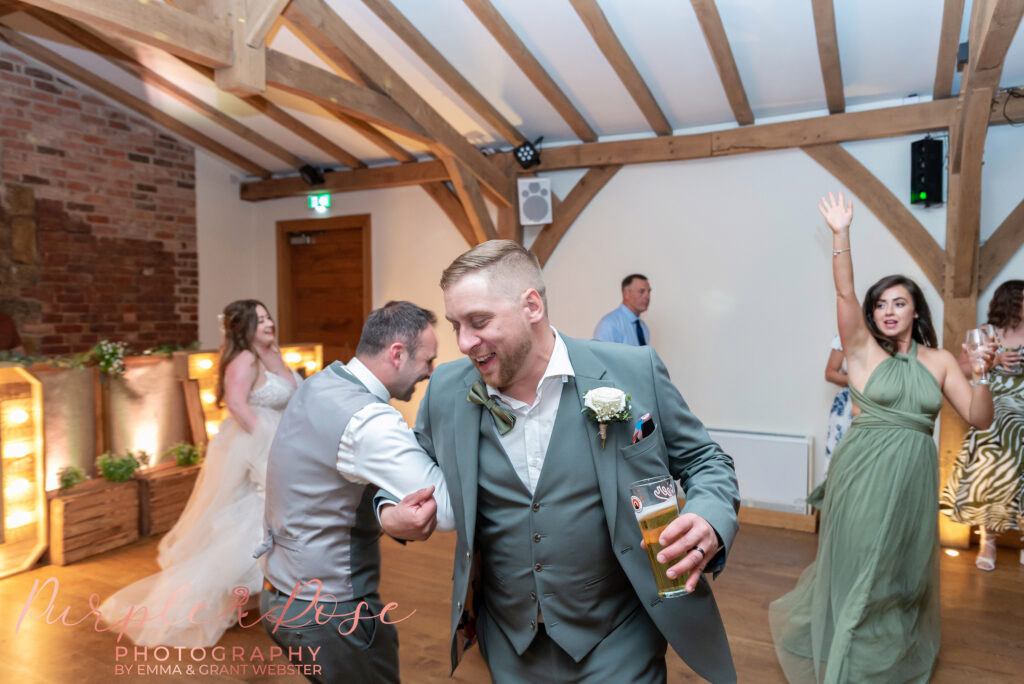 Groom linking arms and dancing with a friend at his wedding at Dodford Manor