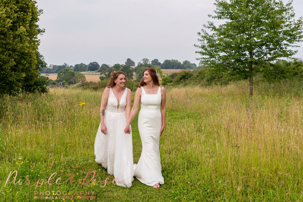 Bride and bride walking hand in hand through a field on their wedding day in Buckinghamshire