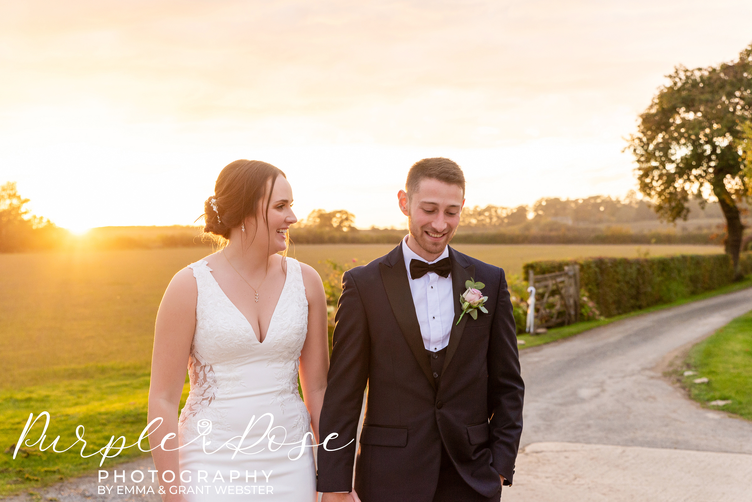 Bride and groom walking hand in hand with golden sunlight behind them on their wedding day in Bicester