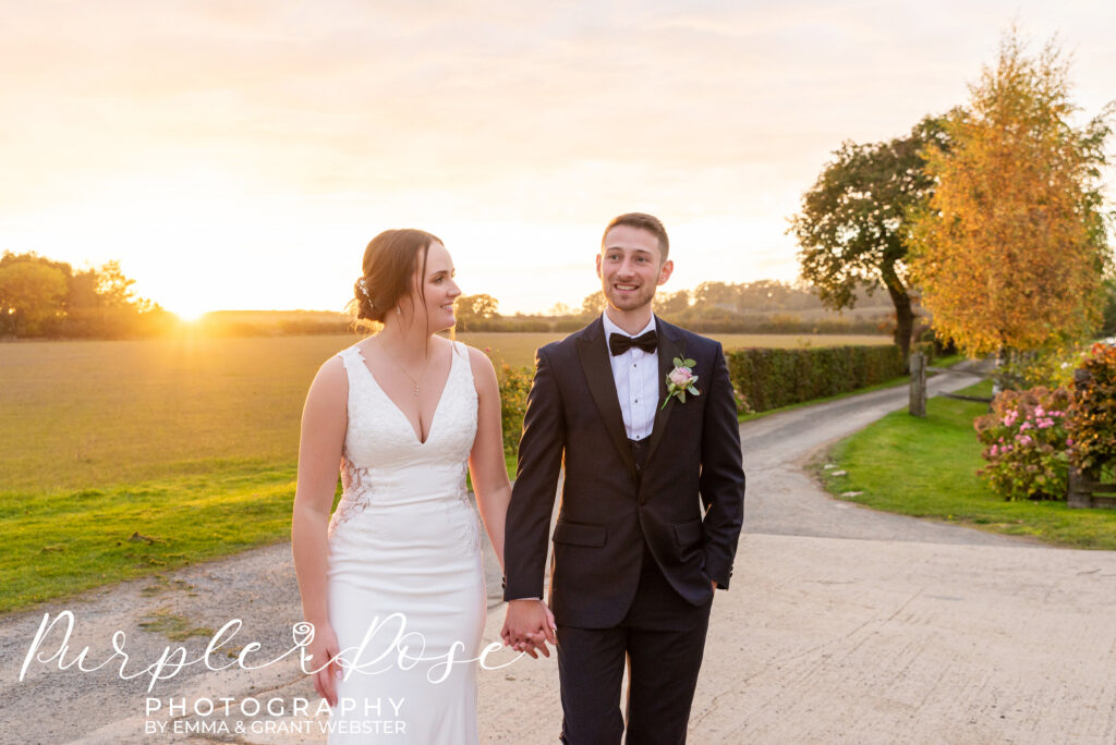 Bride and groom walking hand in hand as the sunsets behind them at their wedding venue in Bicester