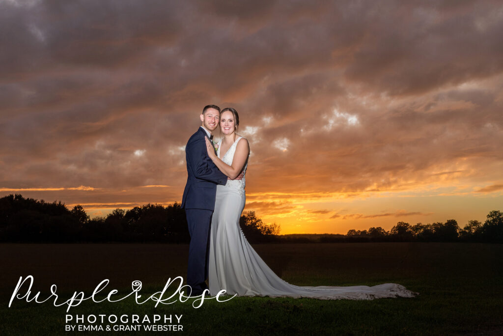 Photo of a bride and groom on their wedding day with a dramatic sunset behind them