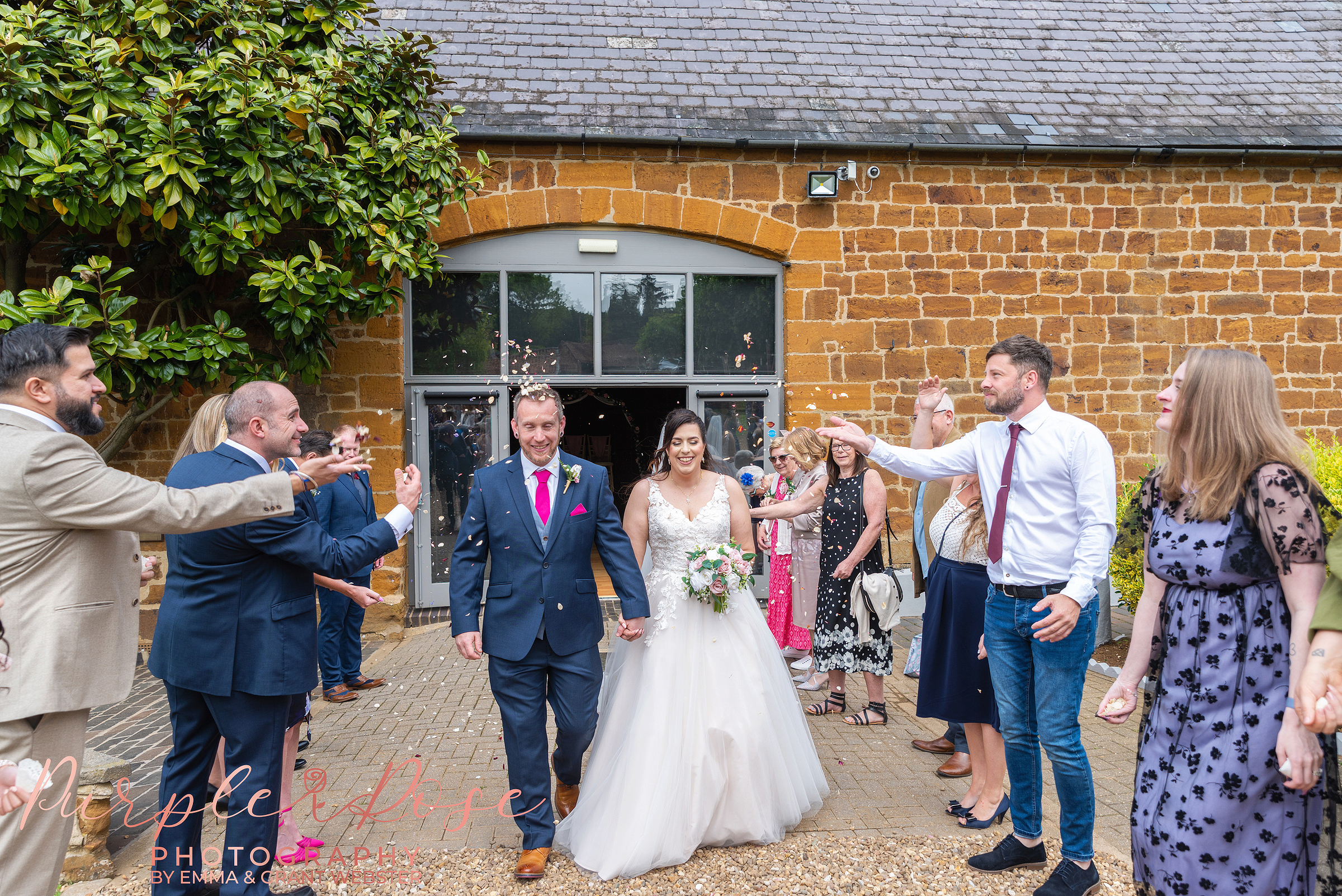 Bride and groom leaving their wedding ceremony as guests throw confetti at their wedding in Northampton