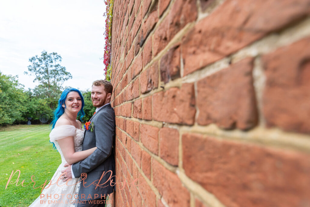 Photo of a bride and groom leaning on abrickway on their wedding day in Milton Keynes