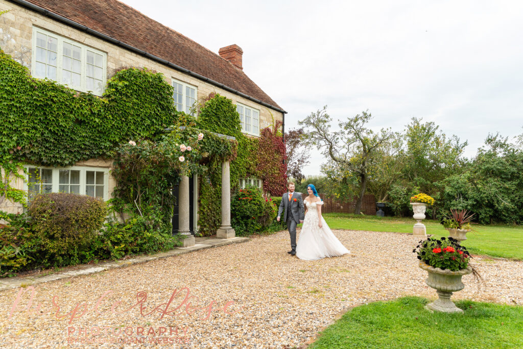 Photo of bride and groom walking in front of a manor house on their weding day in Milton Keynes