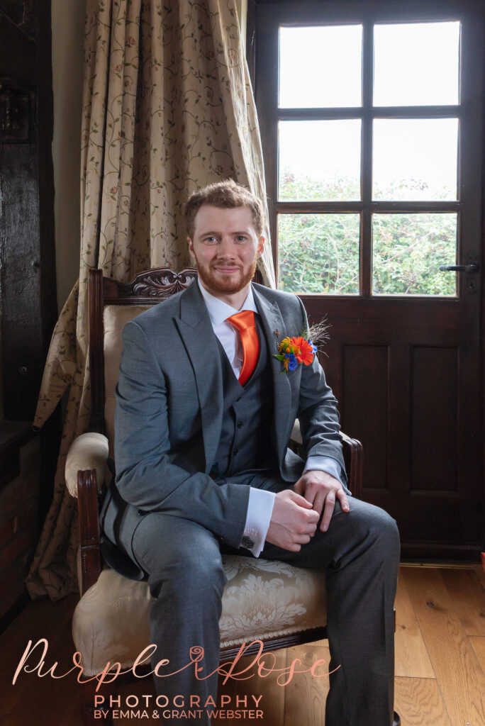 Photo of a groom sat in a chair in front of a window on his wedding day in Milton Keynes