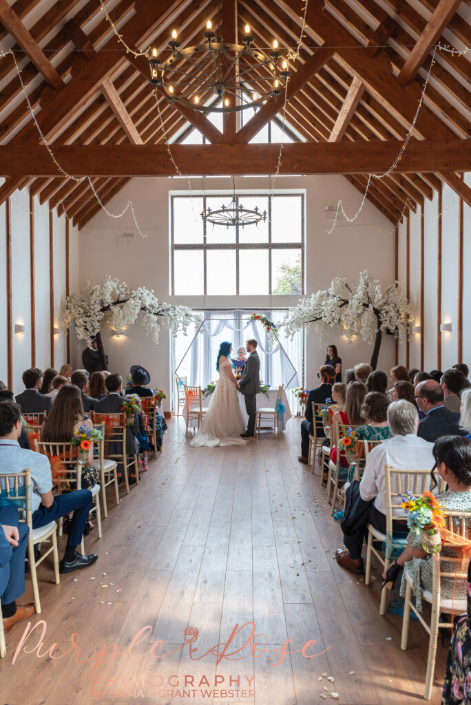 Photo of bride and groom stood holding hands in front of a large window on their wedding day in Milton Keynes