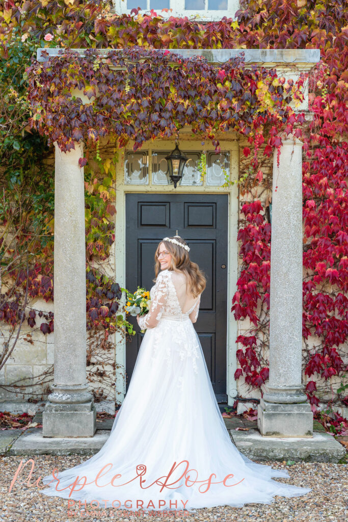 Photo of a bride looking over her shoulder stood in front of an ivy covered dorrway on her wedding day in Milton Keynes