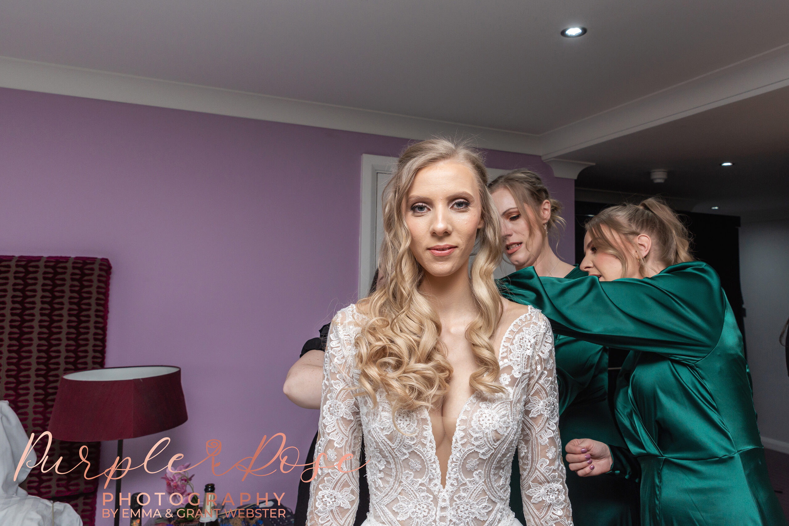 Photo of a bride looking into the camera as her dress is adjusted on her wedding day in Milton Keynes