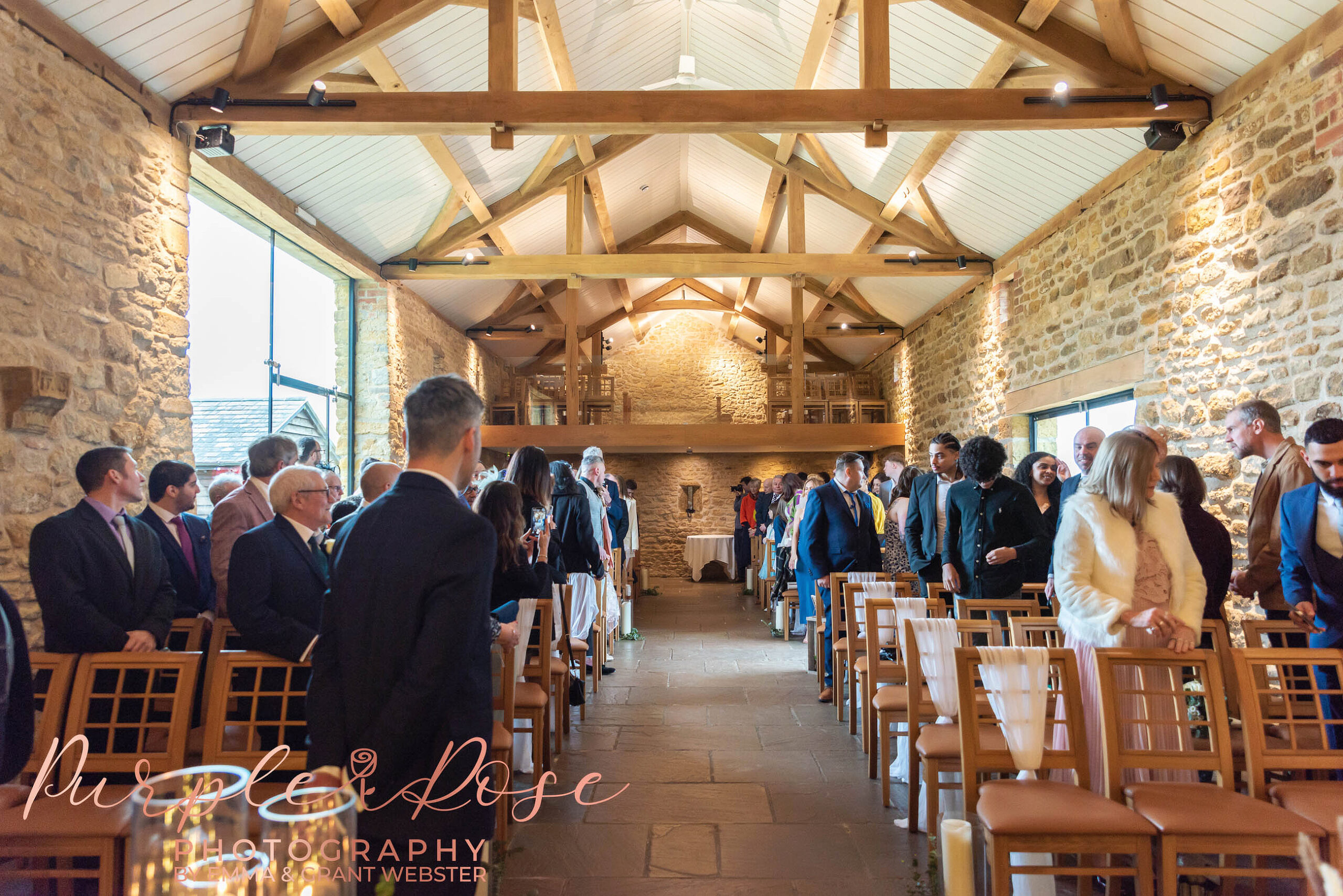 Photo of a groom looking down a barn filled with freinds and family as he waits for his bride to arrive at their wedding in Milton Keynes