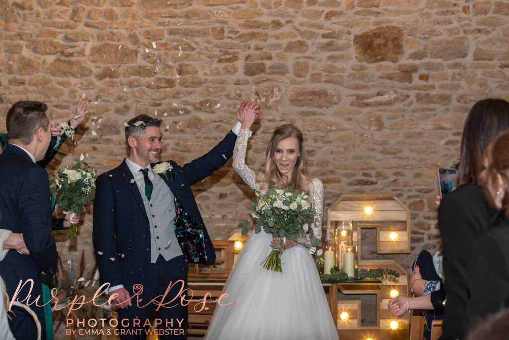 Photo of bride and groom raising their arms in celebration as they leave their wedding ceremony in MIlton Keynes