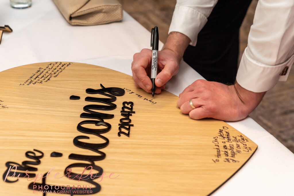 Photo of a wedding guests writing a message on a couples signing board at a wedding in Milton Keynes