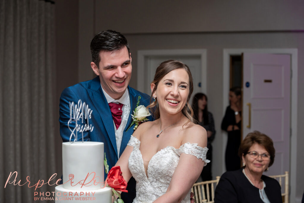 Photo of a bride and groom laughing as they cut their wedding cake in Milton Keynes