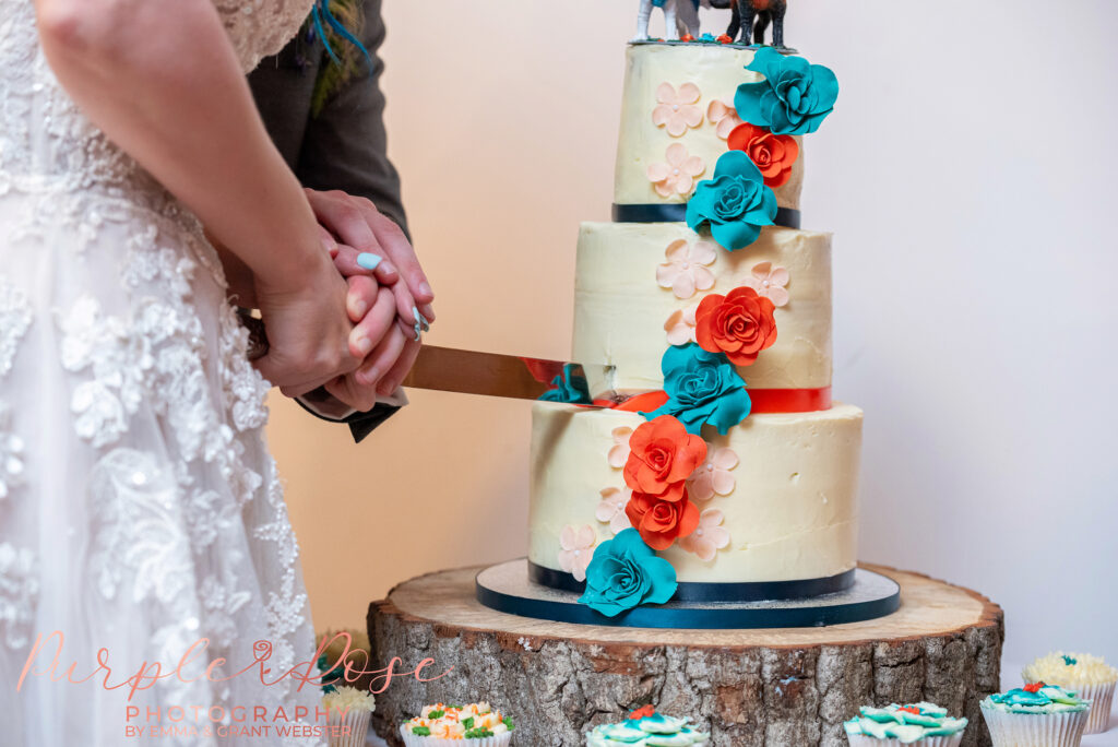 Photo of a 3 tier wedding cake being cut by a bride and groom on their wedding day in Milton Keynes