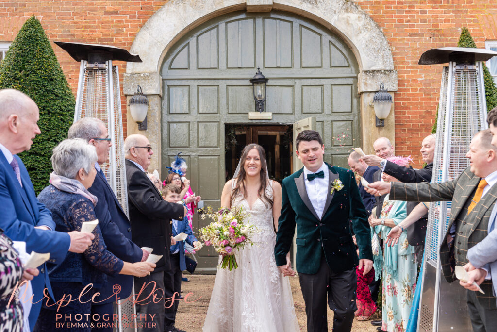 Photo of a bride and groom walking through a confetti tunnel on their wedding day in Northampton