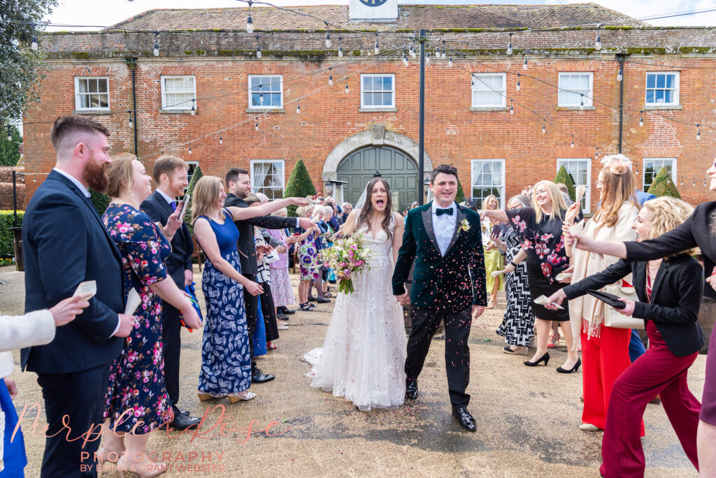 Photo of a bride and groom walking through a confetti tunnel on their wedding day in Northampton