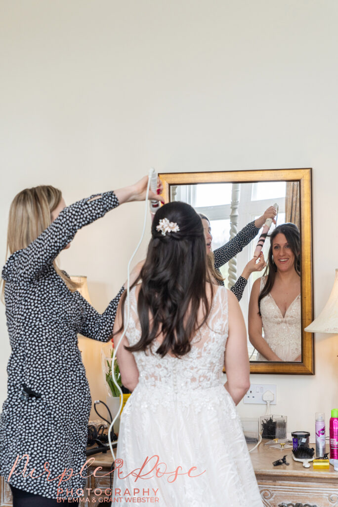 Photo of a bride on her wedding day with her hair stylist adjusting her hair in Northampton