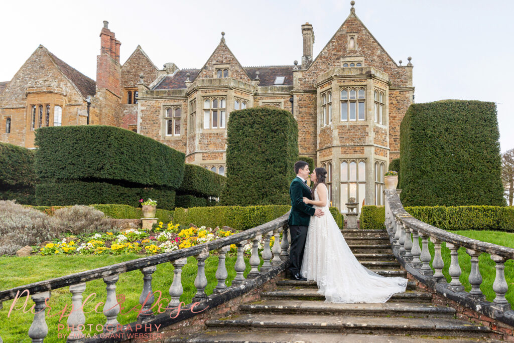 Photo of a bride and groom leaning on a banister of a staircase outside their wedding venue in Northampton