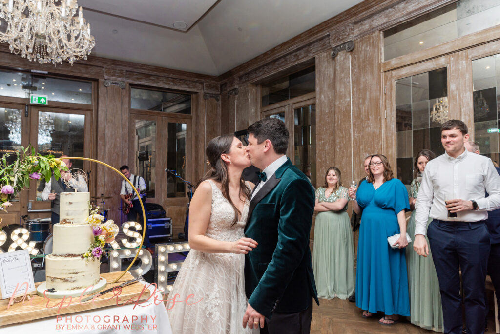 Photo of a bride and groom kissing by their wedding cake at their wedding Northampton