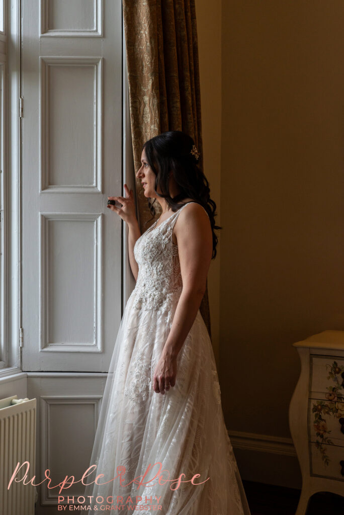 Photo of a bride looking out of a window on her wedding day in Northampton