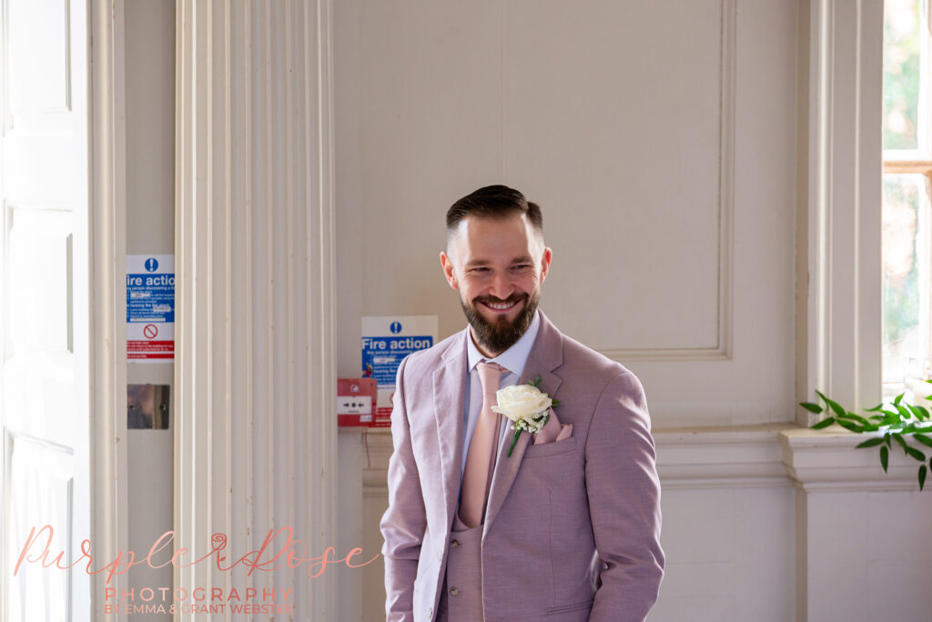Groom smiling at his wedding guests as he waits for the wedding ceremony to start at Chicheley Hall in Milton Keynes