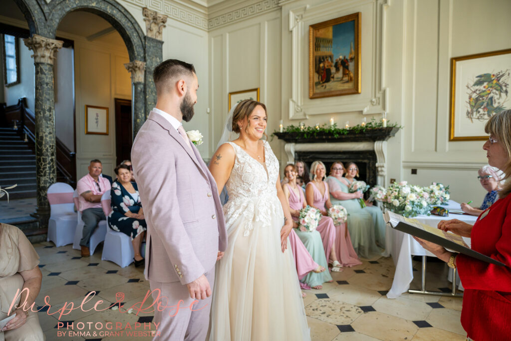 Bride and groom stood side by side holding hands during their wedding ceremony at Chicheley Hall in Milton Keynes