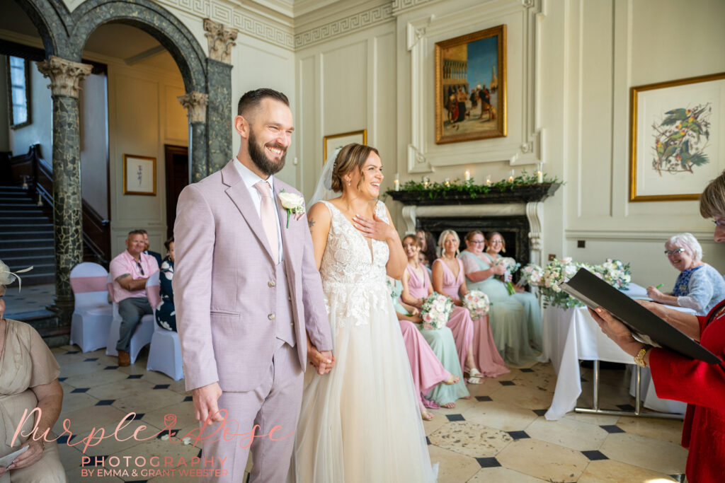 Bride and groom stood side by side holding hands during their wedding ceremony at Chicheley Hall in Milton Keynes