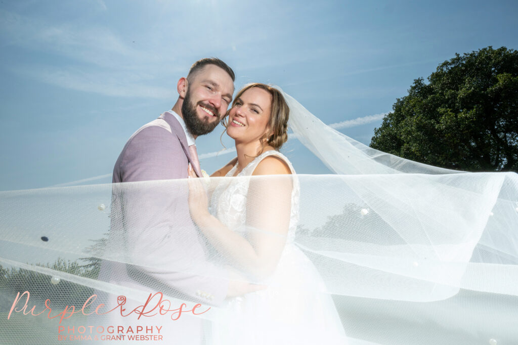 Brides cathedral length veil swirling around her and her groom on their wedding day in Milton Keynes