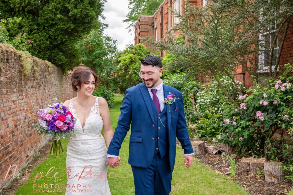 A bride and groom laughing as they stroll through gardens on their wedding day in Milton Keynes