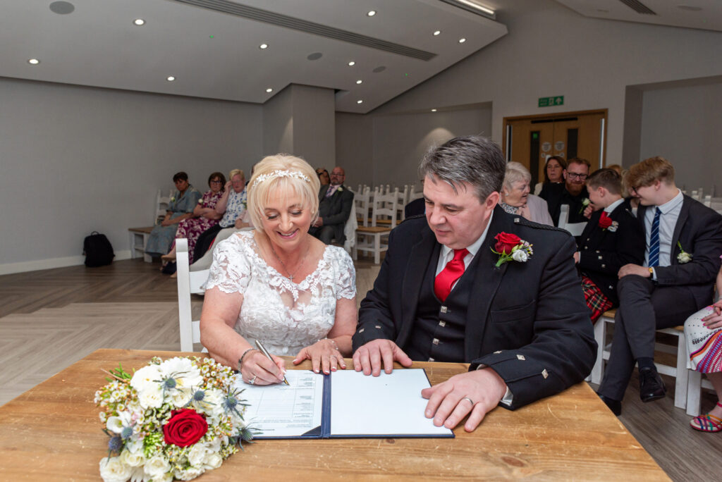 Photo of a bride and groom sighing the register after their wedding at Bride and groom laughing during their wedding ceremony at Milton Keynes Registry Office