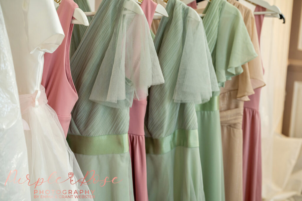 Photo of pink and sage bridesmaid dresses hanging on a rail on a wedding morning at Chicheley Hall in Milton Keynes