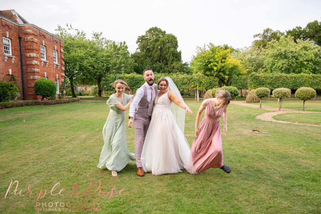 Bride and groom laughing as their children sneak up on them at Chicheley Hall in Milton Keynes