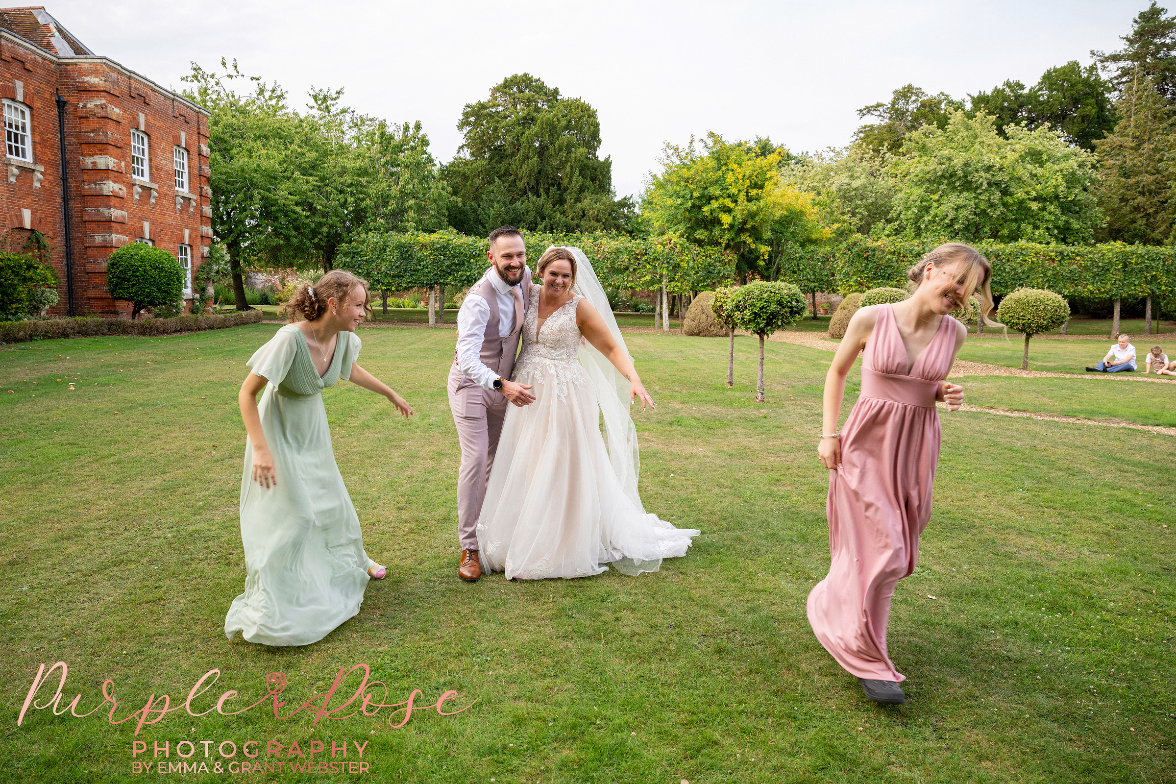 Bride and groom laughing as their children sneak up on them at Chicheley Hall in Milton Keynes