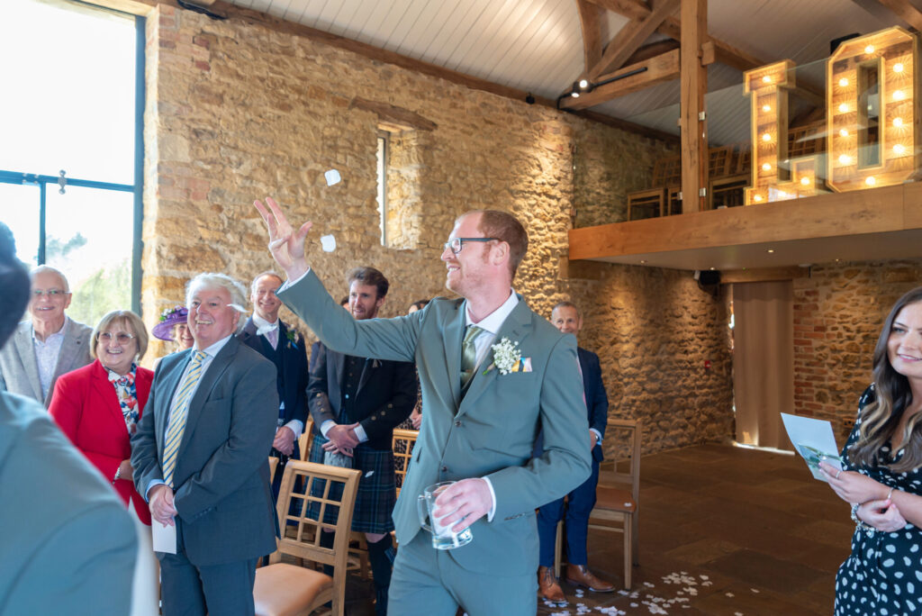 Photo of a groomsman throwing petals as he walks down the aisle at Dodford manor